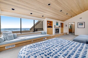 A bedroom with a large bed, a built-in bench with seating, a wooden ceiling, and a view of the ocean. - Sea Ranch 4BR architectural home with ocean views & private hot tub (Sea Ranch)
