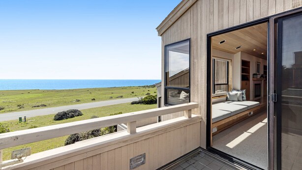 Ein Balkon mit Meerblick, eine Schiebetür zu einem Zimmer mit einem Bett und einem Fenster.