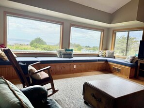 A room with a built-in bench along a large window, a wooden chair, a small table, and a suitcase. - Ocean view home with fireplace, deck, private hot tub & grill (Sea Ranch)