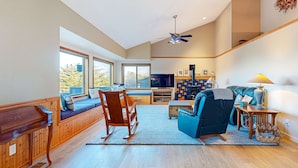 A spacious living room with a large window, a television, a sofa, a rocking chair, and a fireplace. - Sea Ranch 2BR ocean-view home with private hot tub & fireplace (Sea Ranch)