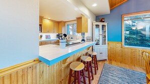 A kitchen with wooden cabinets, a white countertop, and a window with a view. - Sea Ranch 2BR ocean-view home with private hot tub & fireplace (Sea Ranch)