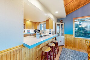A kitchen with wooden cabinets, a white countertop, and a window with a view. - Sea Ranch 2BR ocean-view home with private hot tub & fireplace (Sea Ranch)