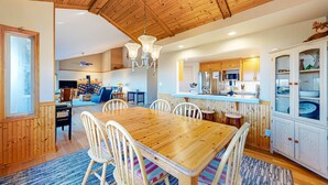 A wooden dining table with chairs, a chandelier, and a kitchen area with cabinets and a microwave. - Sea Ranch 2BR ocean-view home with private hot tub & fireplace (Sea Ranch)