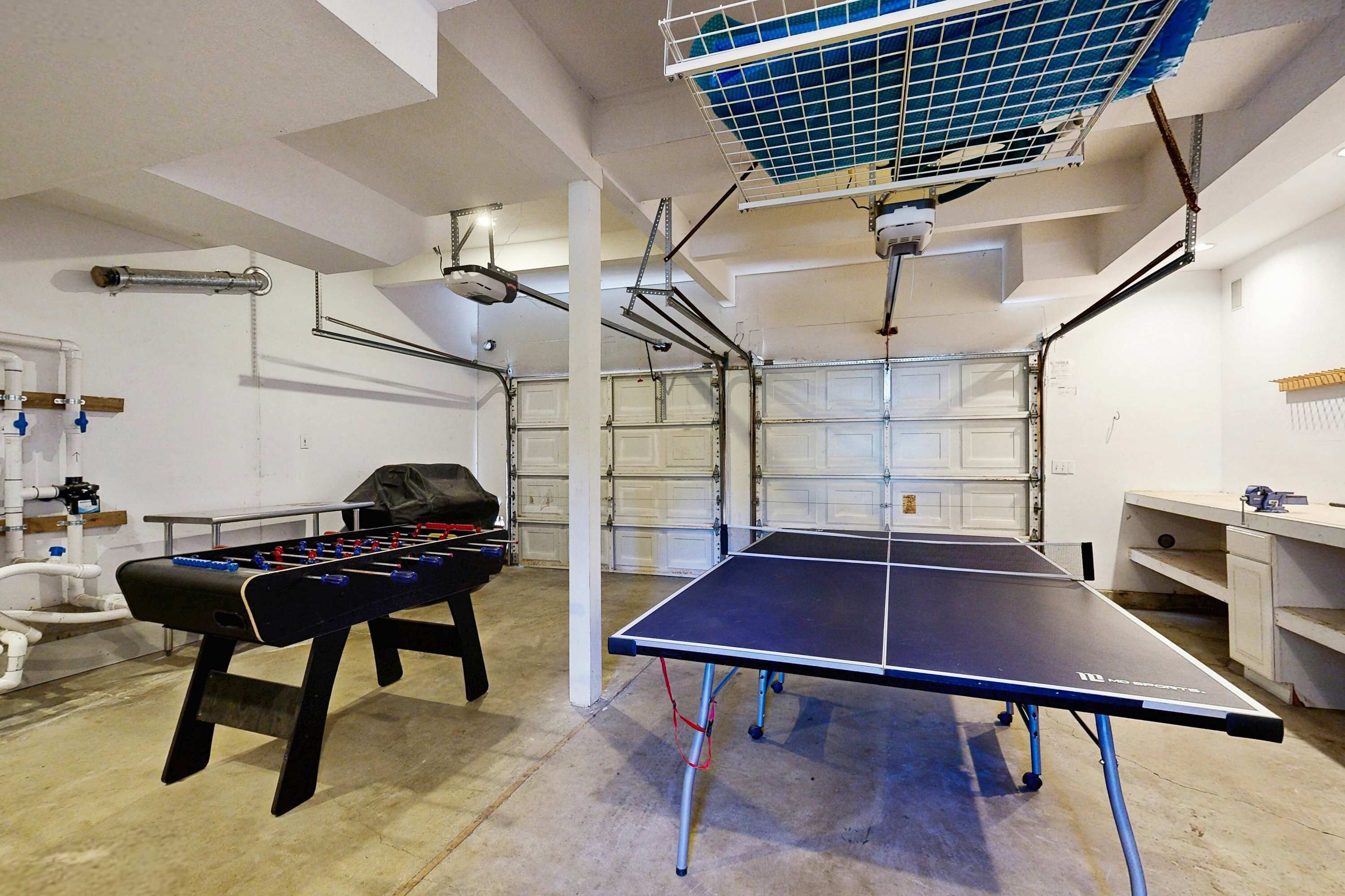 Une table de ping-pong, un baby-foot et un panneau solaire fixé au plafond dans une pièce aux murs blancs et au sol en béton.