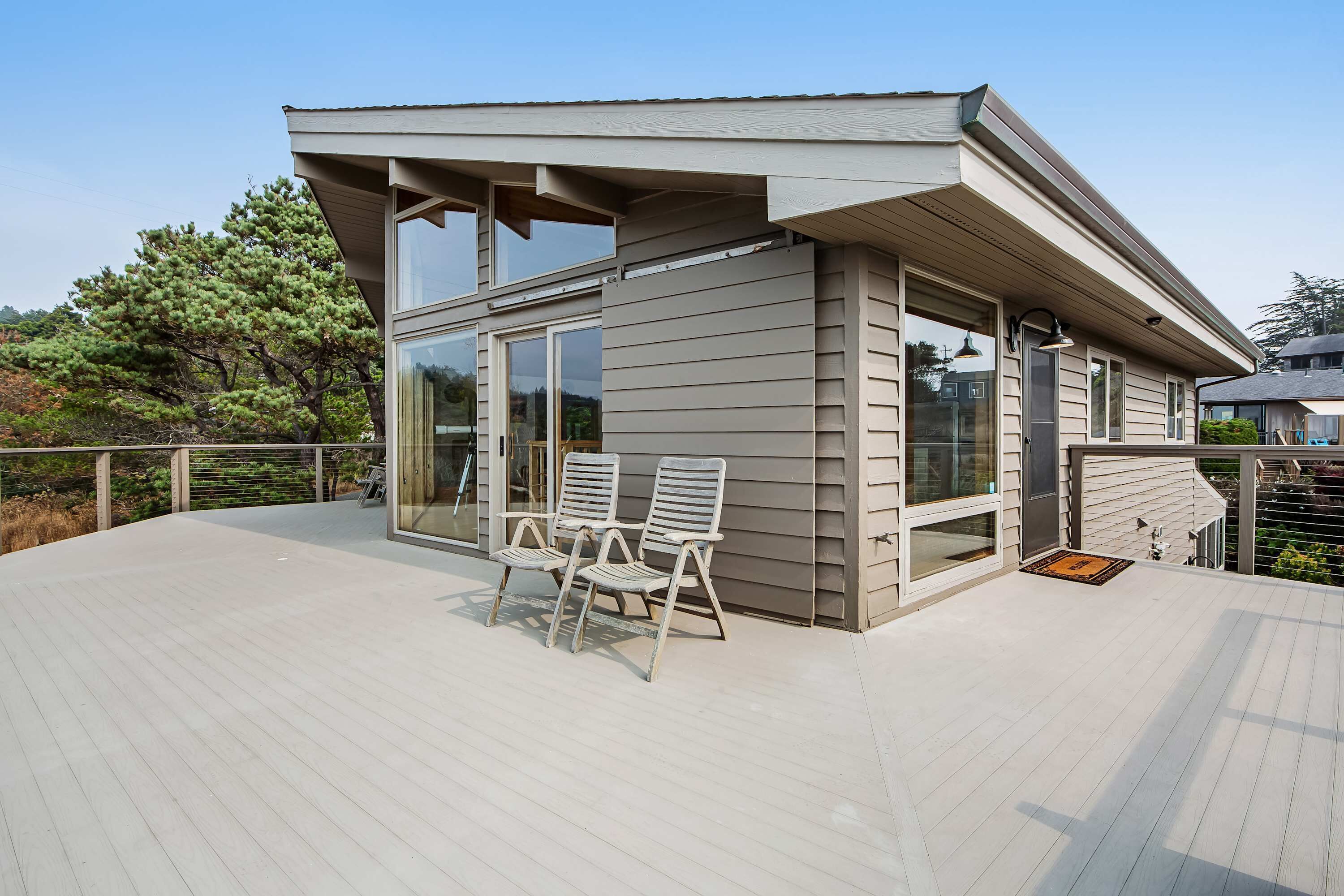 A modern house with a deck, large windows, and two chairs.