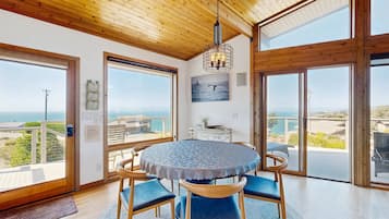 A room with a round table, chairs, a ceiling light, and large windows with a view of the sea.