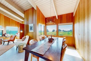 A dining area with a long table, chairs, and a view of the outdoors. - Oceanfront home near Shell Beach & Bluff Trail with deck & ocean views (Sea Ranch)