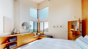 A bedroom with a large bed, a wooden dresser, a seating area with a bench, a round mirror, and a view of the outdoors. - Sea Ranch 3BR oceanfront home near Shell Beach & Bluff Trail (Sea Ranch)