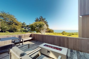 An outdoor deck with a fire feature, seating, and a view of the ocean. - Oceanfront home near Shell Beach & Bluff Trail with deck & ocean views (Sea Ranch)