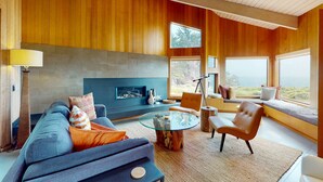 A modern living room with a fireplace, a sofa, a coffee table, and a view through large windows. - Sea Ranch 3BR oceanfront home near Shell Beach & Bluff Trail (Sea Ranch)