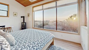 Un dormitorio con un ventanal grande, tragaluces y una cama con ropa de cama estampada.