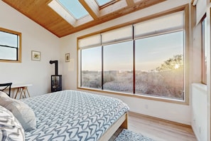 A bedroom with a large window, skylight, and a bed with patterned bedding. - Sea Ranch 3BR hot tub — Meadow home with hot tub & trail ac (Sea Ranch)
