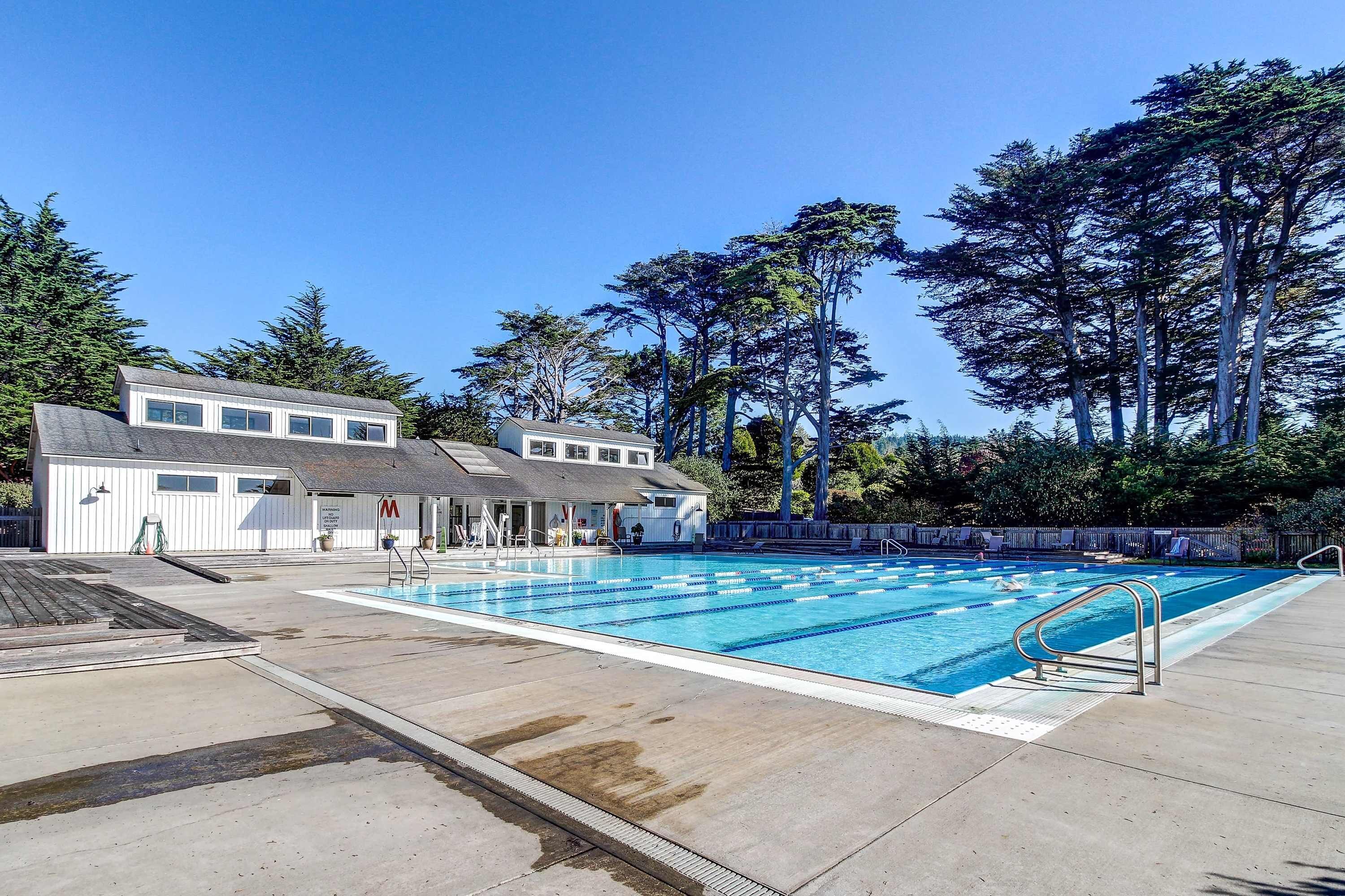 A swimming pool with a diving board, surrounded by buildings and trees.