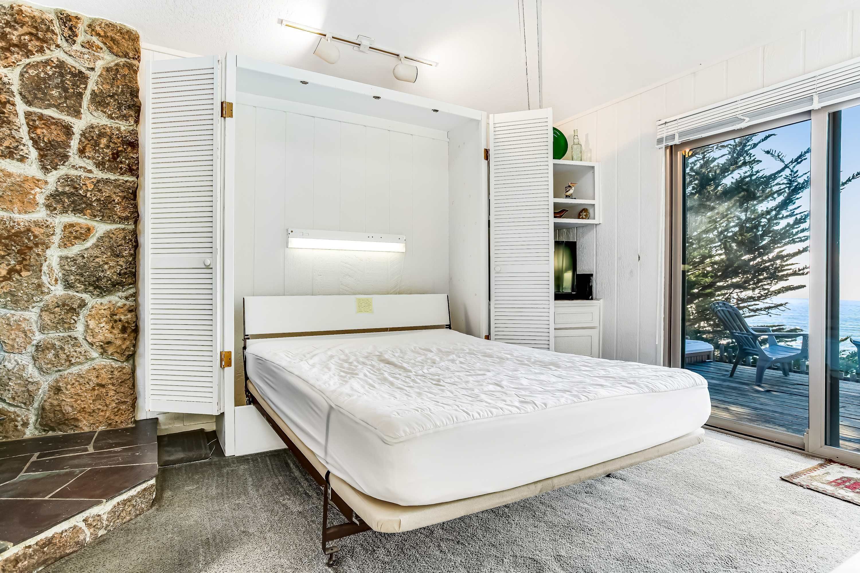 Ein Schlafzimmer mit einem Bett, einer Steinsäule, einer Schiebetür und Blick ins Freie.