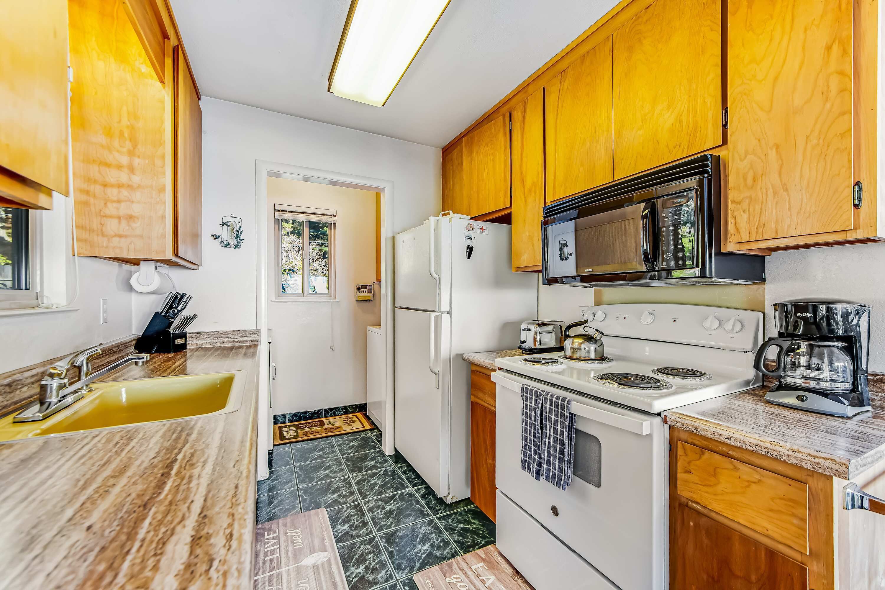 A compact kitchen with wooden cabinets, a white refrigerator, a microwave, a stove, and a sink.