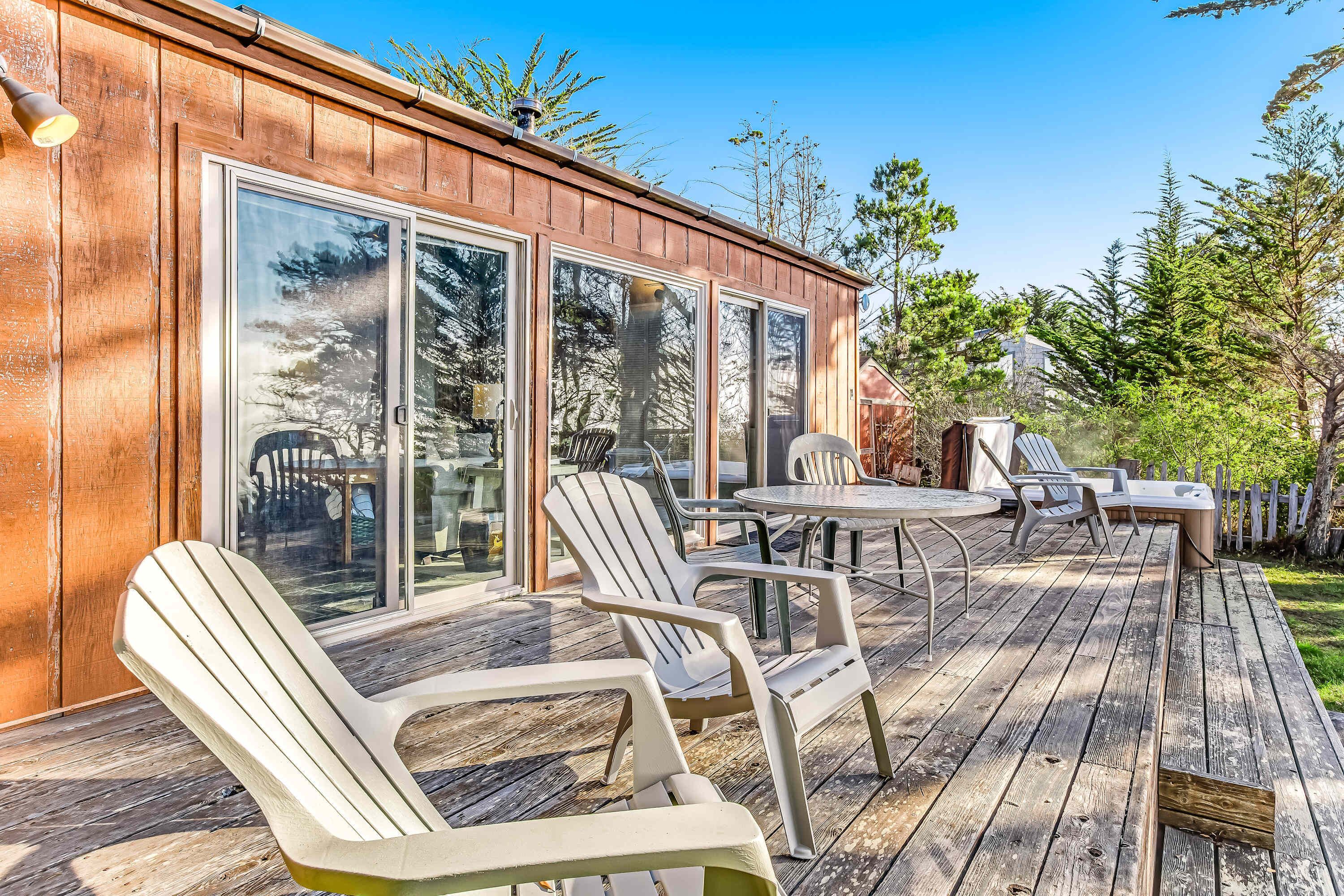 A wooden deck with Adirondack chairs and a table, a sliding glass door, and a view of trees.