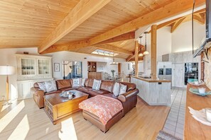 A spacious living area with a wooden ceiling, a brown leather sofa, a wooden coffee table, and a kitchen in the background. - Sea Ranch 3BR dog-friendly home with cove views & private hot tub (Sea Ranch)