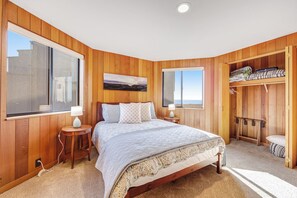 A bedroom with a large bed, wooden walls, a window, and a wardrobe. - Sea Ranch 3BR dog-friendly home with cove views & private hot tub (Sea Ranch)