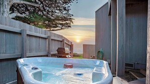 Uma banheira de hidromassagem com deck de madeira, churrasqueira e vista para o pôr do sol.