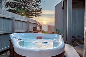 A hot tub with a wooden deck, a barbecue grill, and a view of the sunset. - Oceanfront retreat with private hot tub steps from Pebble Beach (Sea Ranch)