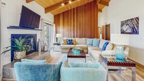A living room with a fireplace, wooden ceiling beams, a sofa set, and a television. - Gualala 3BR updated coastal home with ocean views & private deck (Gualala)