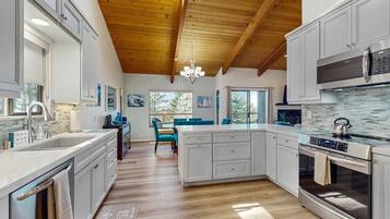 A modern kitchen with wooden beams, a central island, stainless steel appliances, and a dining area with blue chairs.