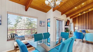 A modern interior with a glass dining table, blue upholstered chairs, wooden beams, and large windows. - Gualala 3BR updated coastal home with ocean views & private deck (Gualala)