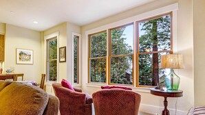 A living room with large windows, a sofa, two armchairs, and a lamp on a side table. - Sea Ranch 2BR forested home on the hillside — dog friendly (Sea Ranch)