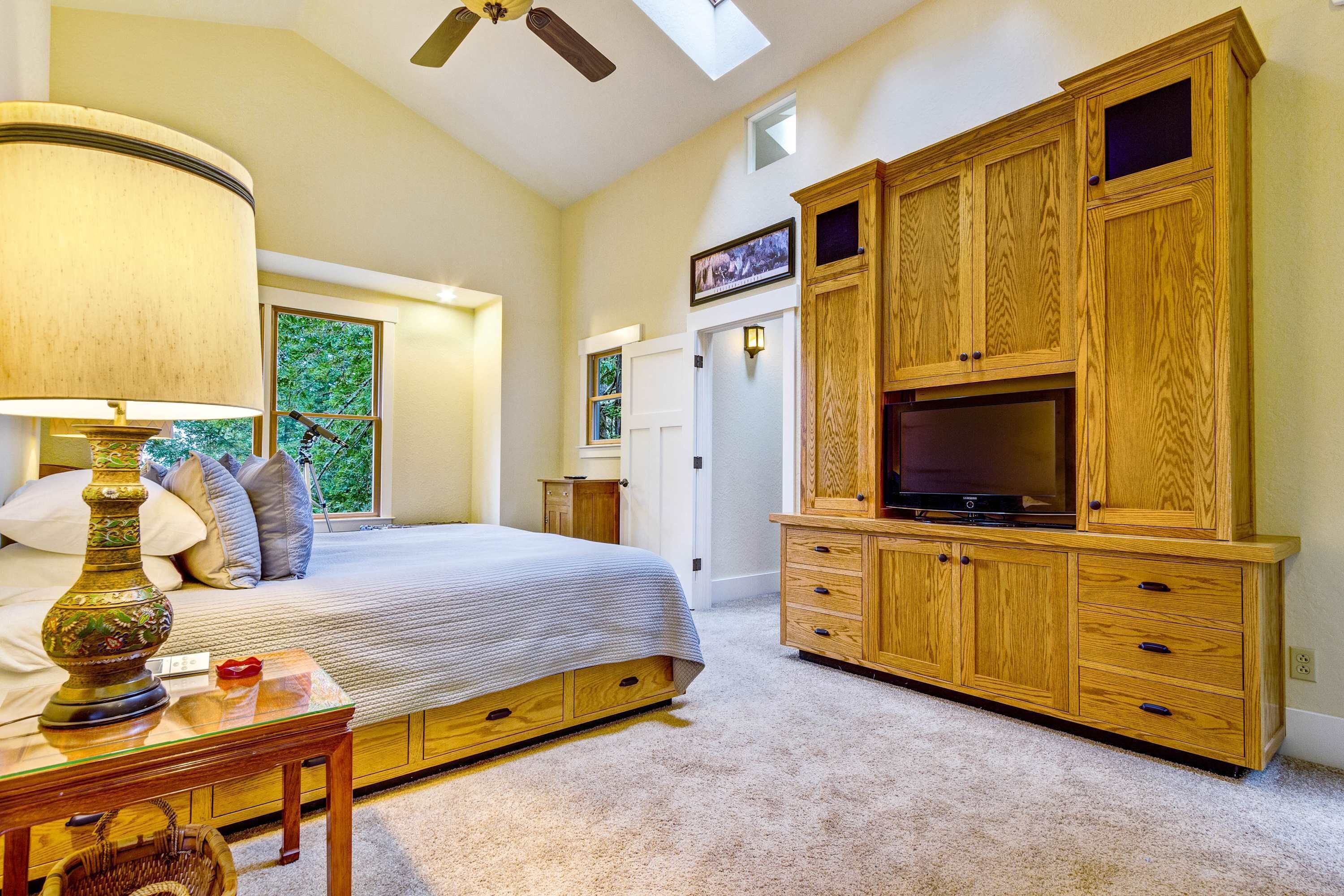 A bedroom with a bed, a TV cabinet, a lamp, and a window.