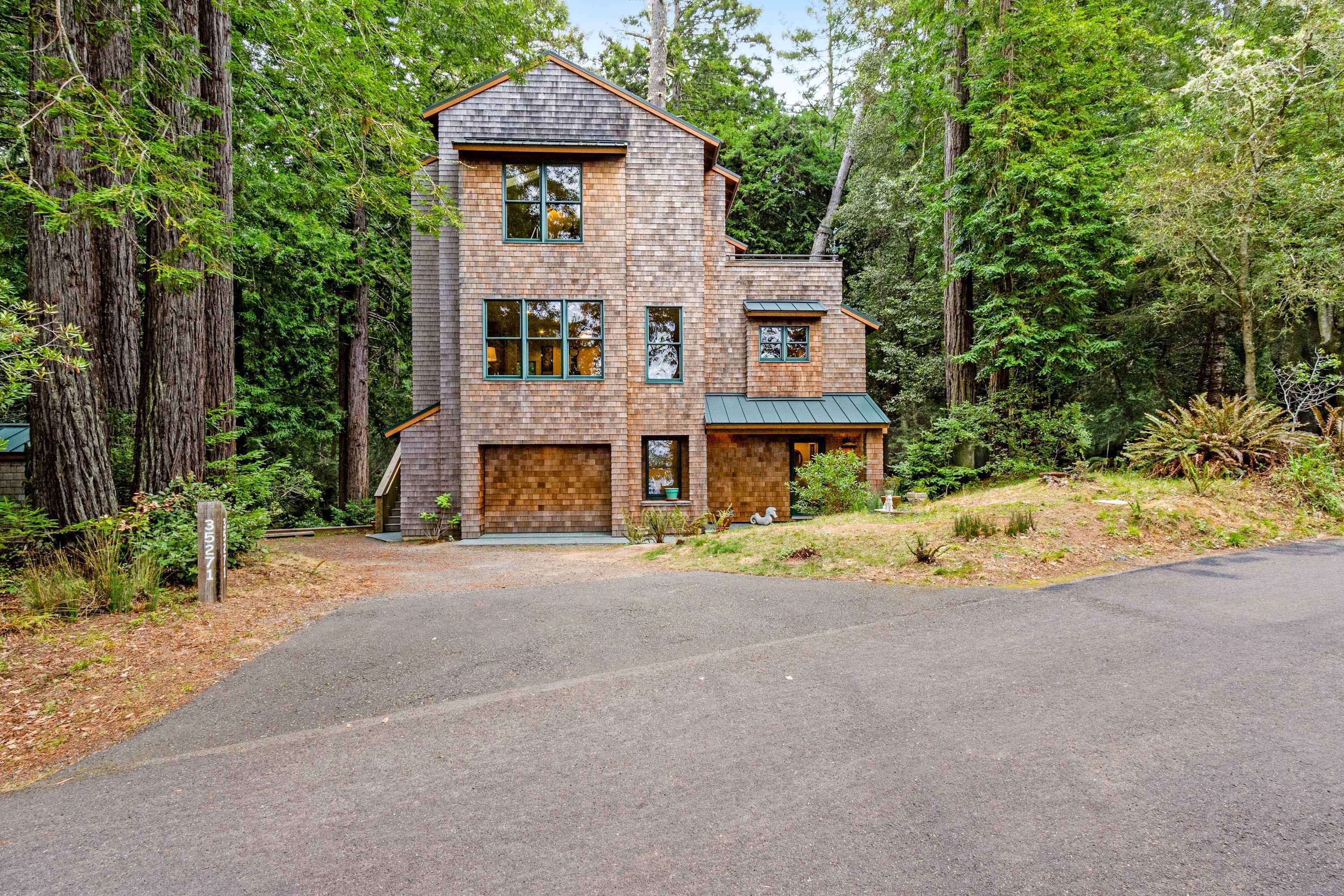 A two-story wooden house with a front porch, surrounded by tall trees.