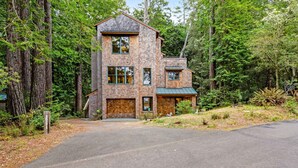 A two-story wooden house with a front porch, surrounded by tall trees. - Sea Ranch 2BR forested home on the hillside — dog friendly (Sea Ranch)