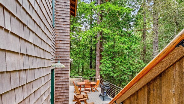 A deck with wooden furniture, a grill, and a view of a forest. - Sea Ranch 2BR forested home on the hillside — dog friendly (Sea Ranch)