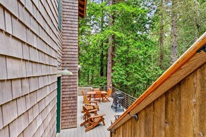 Une terrasse dotée de meubles en bois, d’un barbecue et offrant une vue sur une forêt.