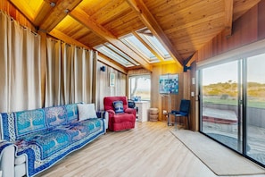 A room with a wooden ceiling, a sofa, a red chair, a TV, and a large window. - Sea Ranch 2BR ocean-view home with hot tub near Shell Beach (Sea Ranch)