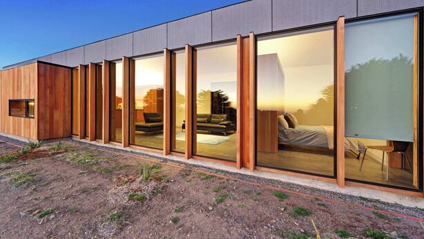 Een modern gebouw met grote glazen deuren, een houten gevel en een zichtbaar interieur met meubilair.