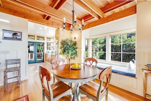 A dining area with a round wooden table, four chairs, a chandelier, and a view of the outdoors through large windows. - Gualala 2BR ocean views — Gualala craftsman home with ocean v (Gualala)