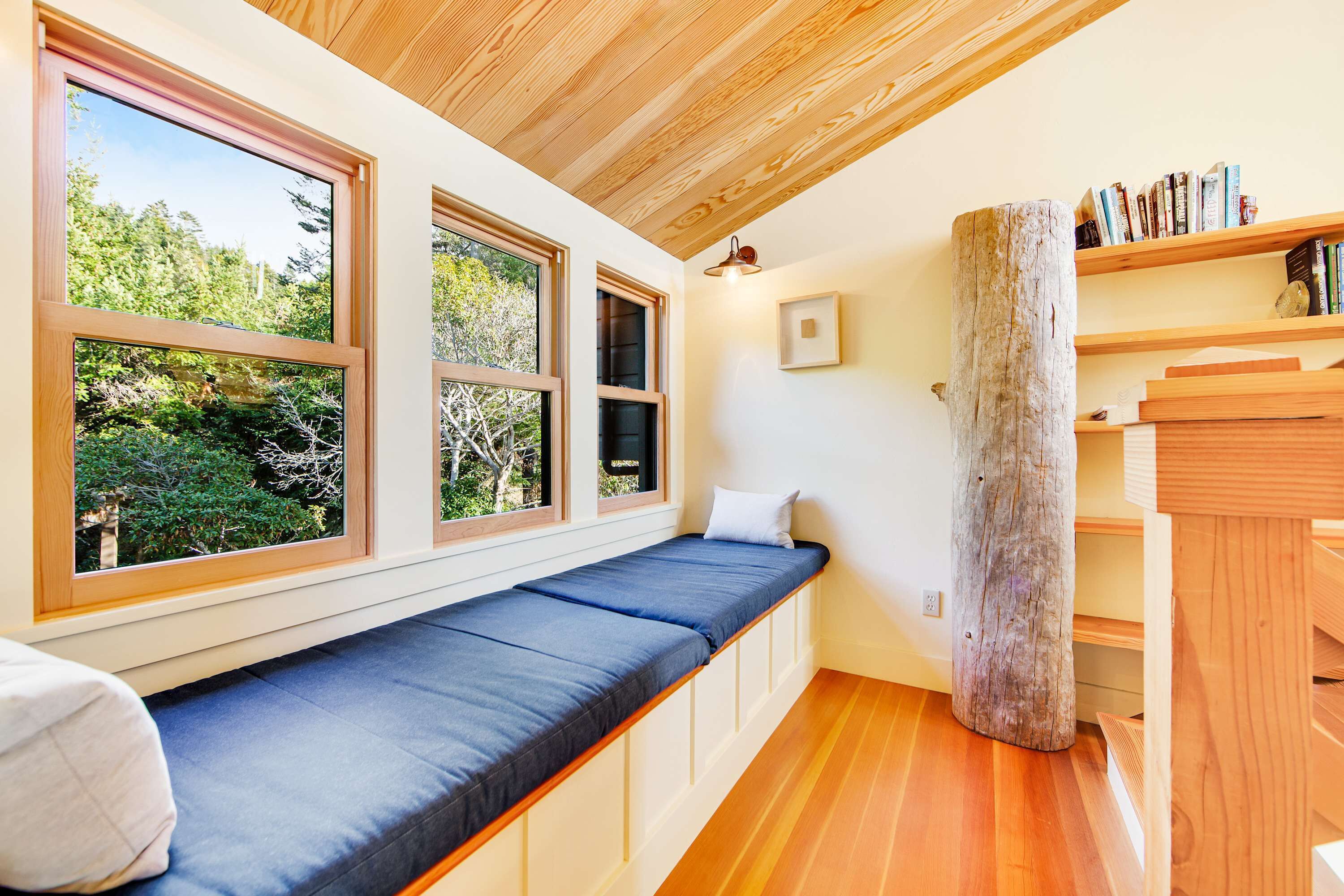 A room with a built-in bench, large windows, a wooden post, and a bookshelf.