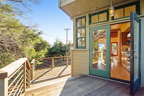 A wooden deck with a glass door leading to a kitchen area. - Gualala 2BR ocean views — Gualala craftsman home with ocean v (Gualala)