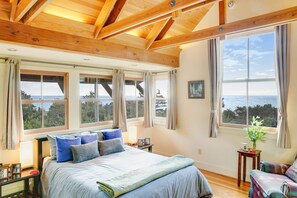 A bedroom with a large bed, multiple windows, and a view of the sea. - Gualala 2BR ocean views — Gualala craftsman home with ocean v (Gualala)