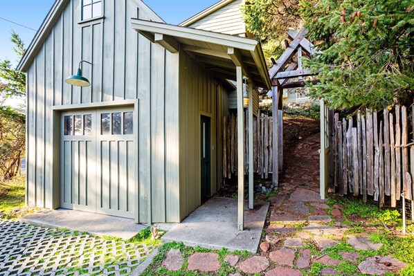 A small, single-story building with a porch, a wooden fence, and a stone pathway leading to the entrance. - Gualala 2BR craftsman home with ocean views, deck & EV charger (Gualala)