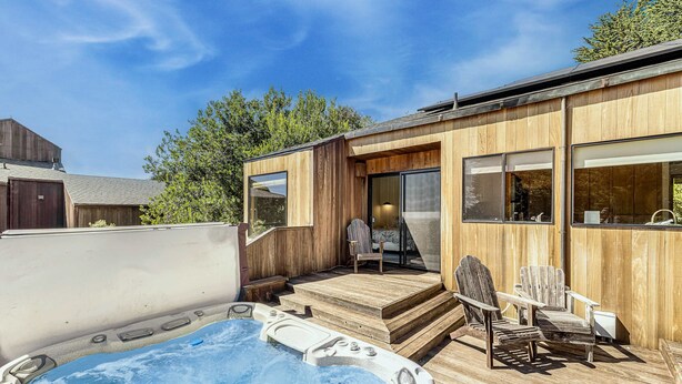 En træterrasse med jacuzzi, udendørs møbler og en skydedør, der fører til et overdækket område.