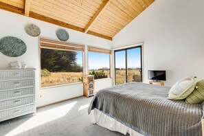 Ein Schlafzimmer mit großem Fenster, einem Bett, einem Schminktisch und einem Fernseher.