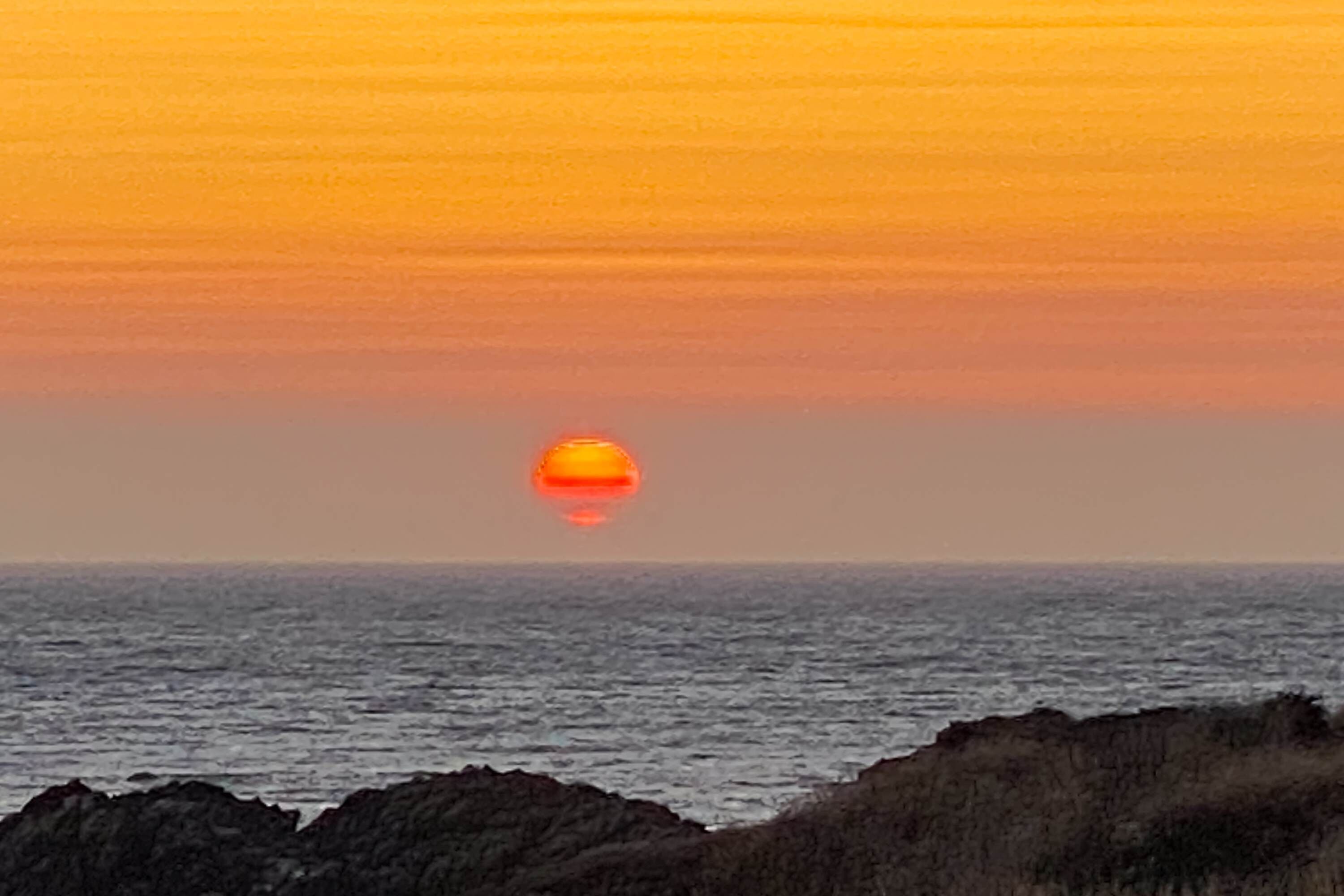 A sunset over the ocean with rocky coastline.