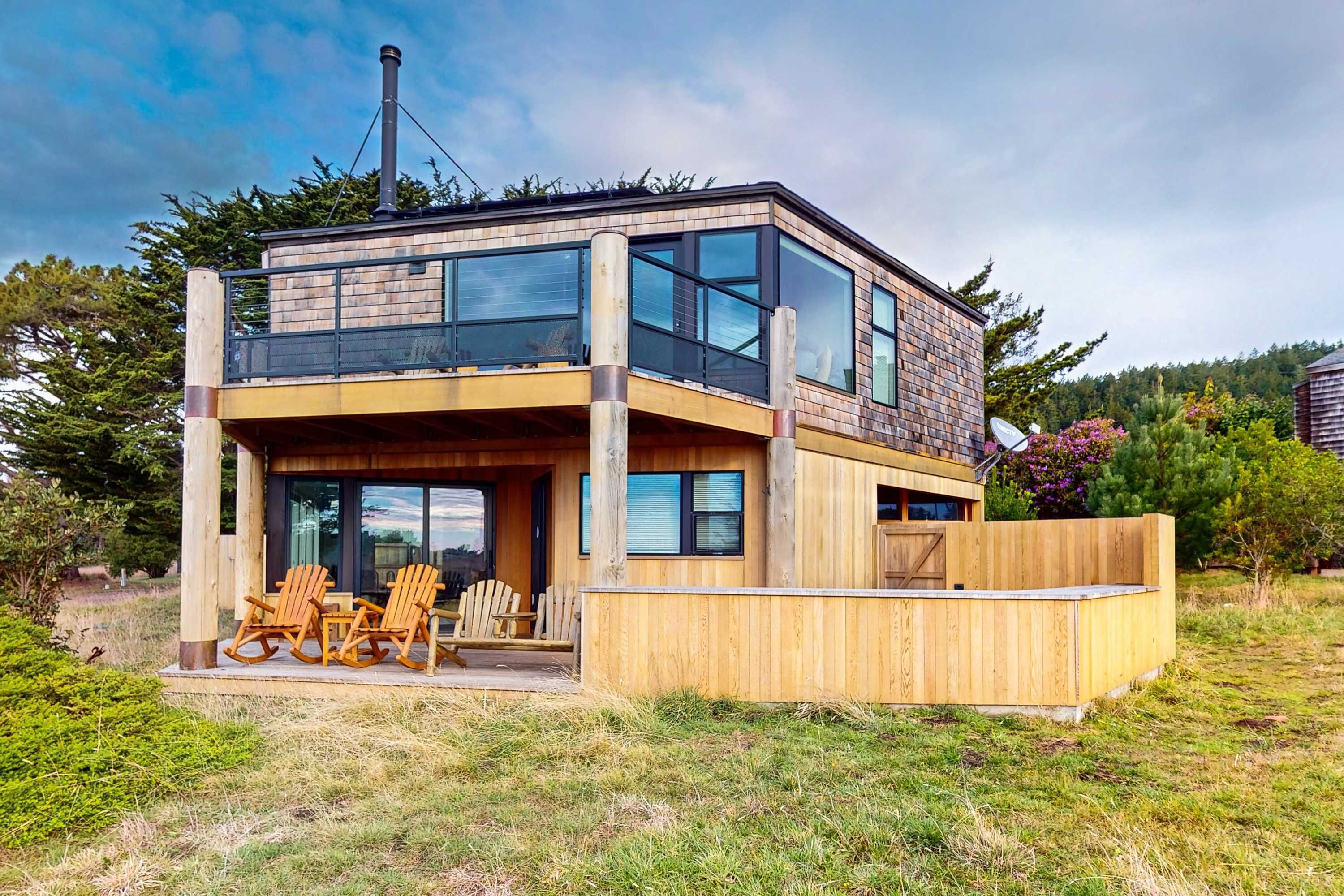 A modern two-story house with a wooden deck, large windows, and a chimney.