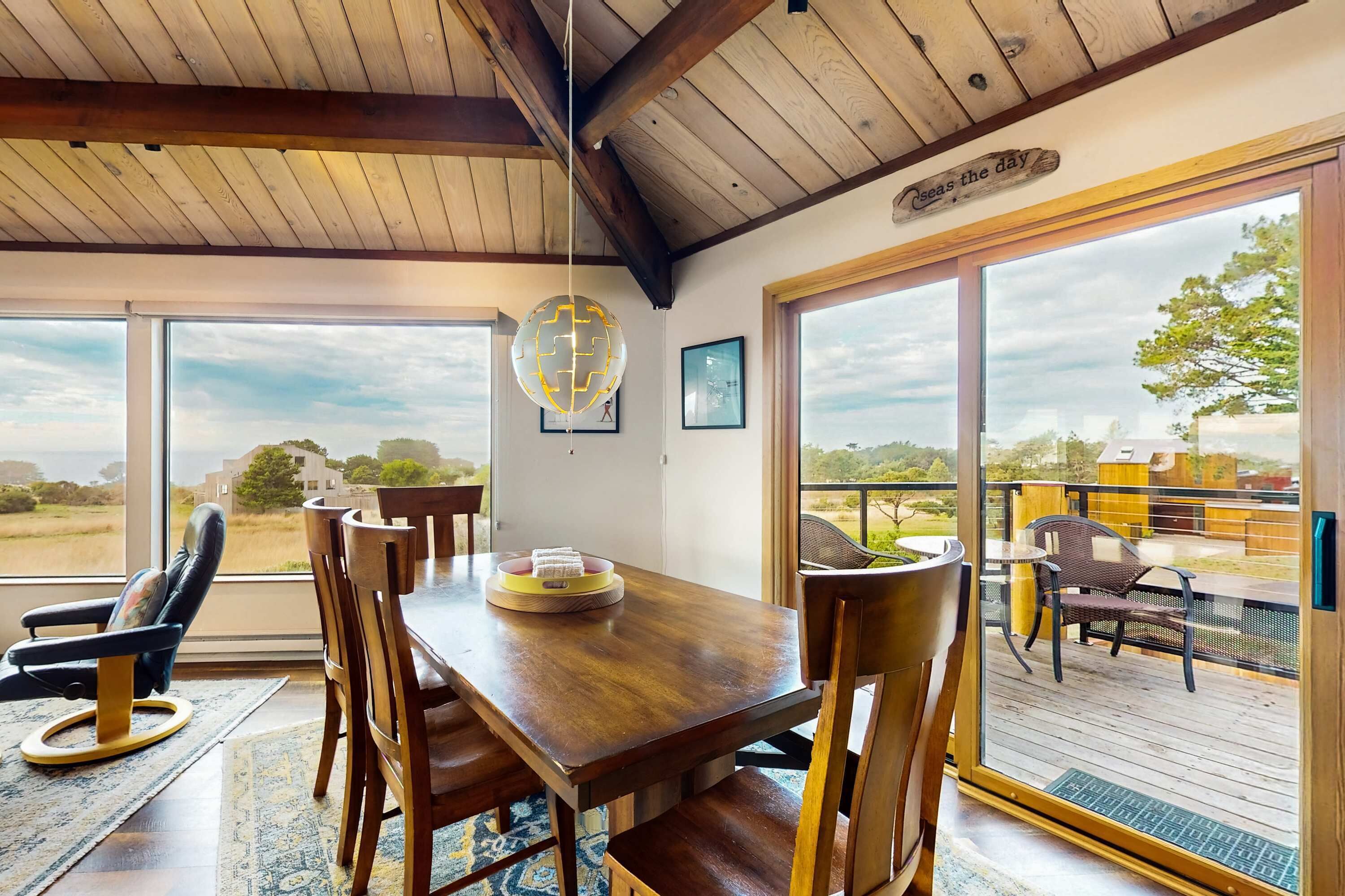 A dining area with a wooden table and chairs, a hanging light fixture, and large sliding glass doors leading to an outdoor deck.