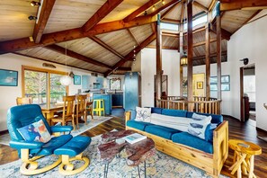 A spacious living area with a wooden ceiling, a blue sofa, a wooden coffee table, and a dining area with a yellow chair. - Newly remodeled hexagon home with hot tub, dogs welcome (Sea Ranch)
