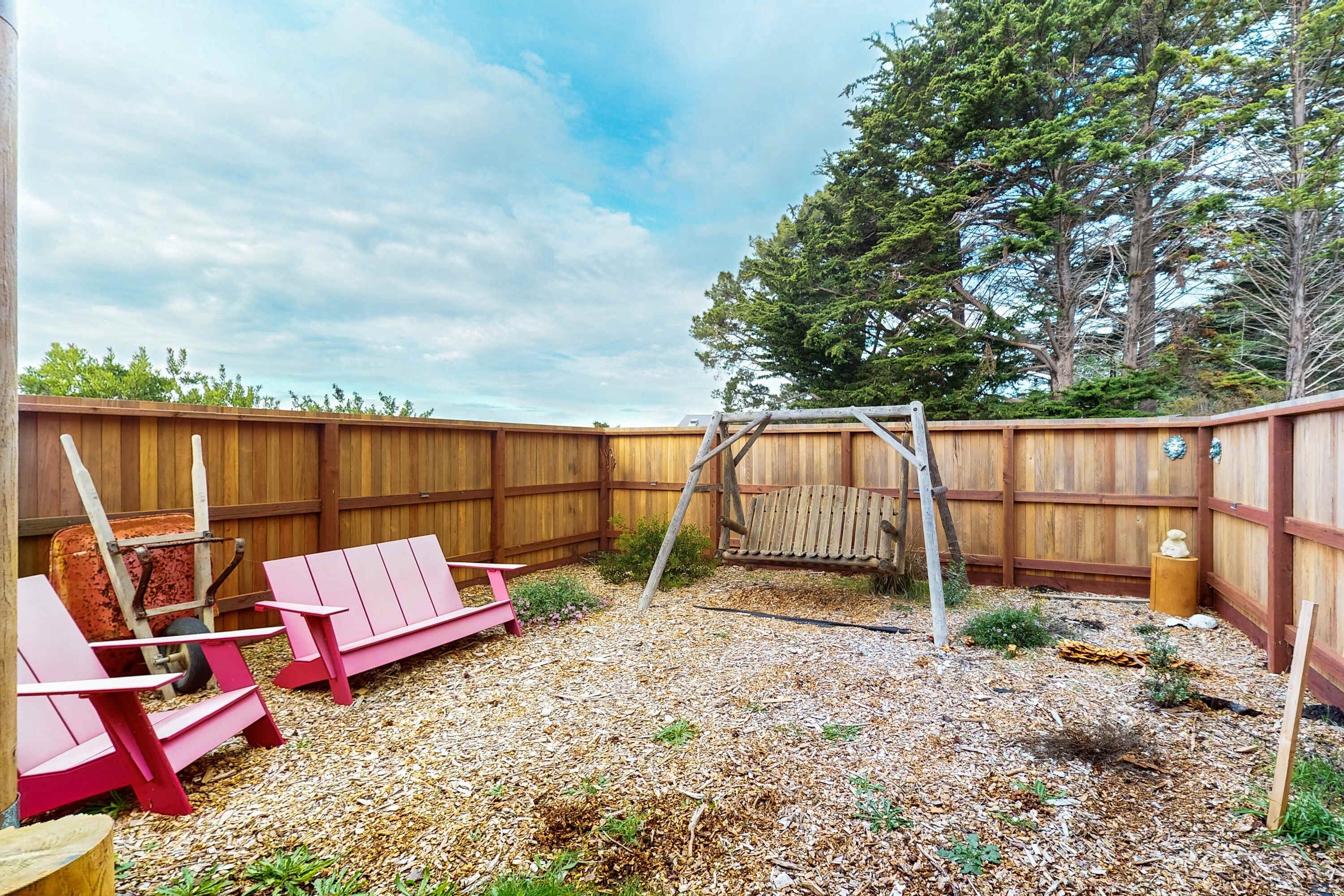 Un jardin avec une clôture en bois, une balançoire et deux fauteuils Adirondack roses.