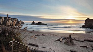 A beach with a sunset, rocky formations, and a metal staircase leading down to the shore. - Gualala 2BR oceanfront blufftop home with hot tub — sleeps 4 (Gualala)