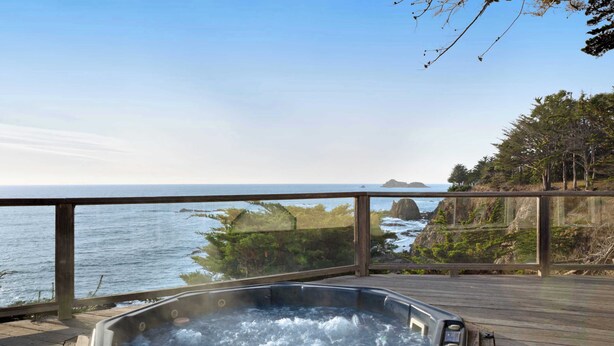 A hot tub on a wooden deck with a view of the ocean and rocky coastline. - Gualala 2BR oceanfront blufftop home with hot tub — sleeps 4 (Gualala)