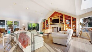 A spacious living room with a fireplace, a large bookshelf, and a painting on the wall. - Gualala 2BR oceanfront blufftop home with hot tub — sleeps 4 (Gualala)